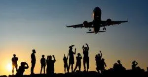 A Dynamic Silhouette Of People Photographing An Airplane During A Vibrant Sunset.