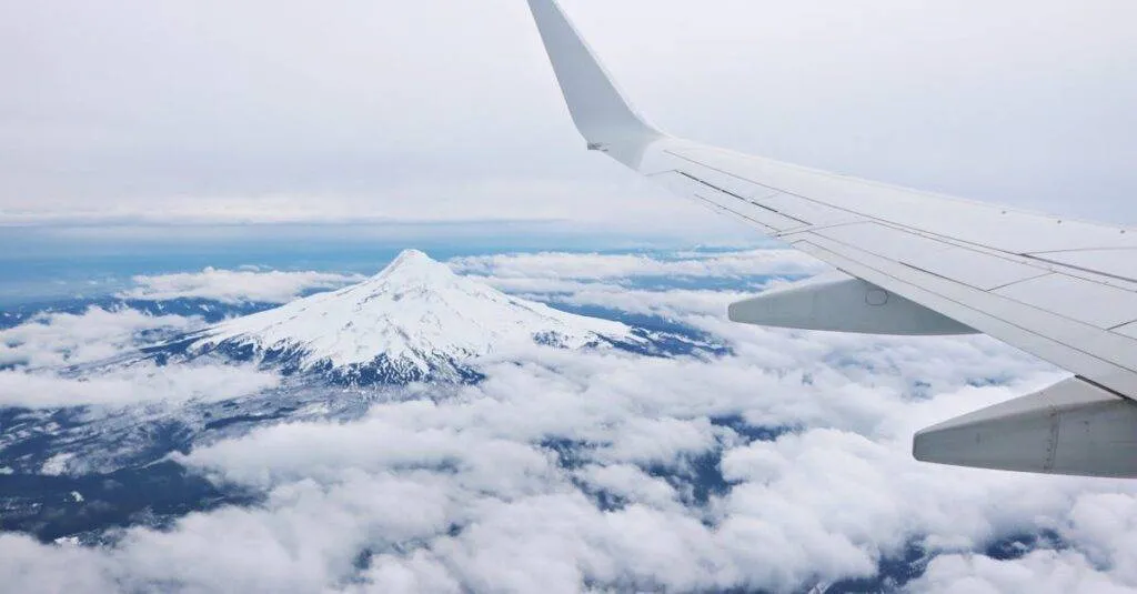 Mountain Peak And Airplane Wing Seen From Above The Clouds, Showcasing A Beautiful Aerial View.