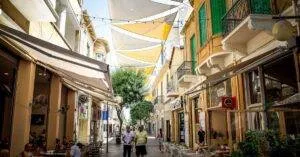 Bustling Street In Nicosia, Cyprus With Cafes, Shops, And People Under Colorful Shades.