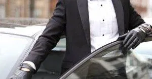 Well-Dressed Man In A Tuxedo Standing Confidently By His Car In An Urban Setting.
