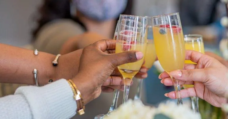 A Diverse Group Toasting With Mimosas In Washington, Dc Indoors.