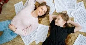 Mother And Daughter Lying On Floor With Sheet Music, Smiling And Looking At Each Other.