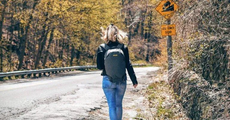 A Woman With A Backpack Walks Along A Scenic Forest Road In Spring, Enjoying An Outdoor Hike.