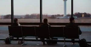 People Sitting In Airport Terminal, Watching Runway Scenes Through Large Windows.