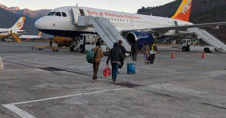 Passengers Boarding A Royal Bhutan Airlines Airbus A319 At Paro Airport Against Mountain Backdrop.