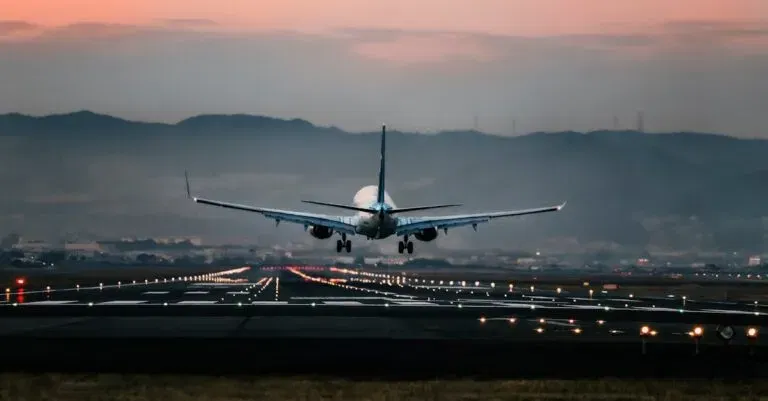 Dramatic View Of A Commercial Airplane Landing On A Runway At Sunset With Mountains In The Background.