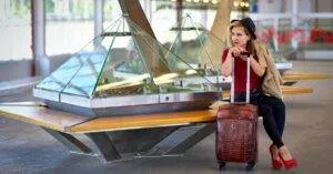Fashionable Woman With Luggage Sitting In A Modern Airport Lobby, Waiting For Her Flight.