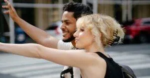 A Cheerful Couple Waves For A Ride On A Sunny Urban Street. Perfect For Lifestyle Themes.