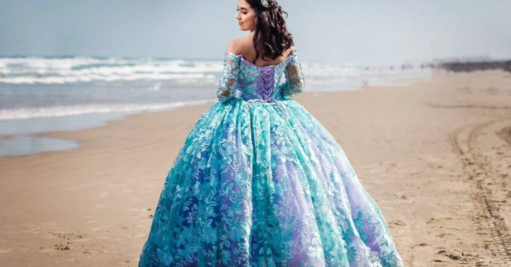 A Woman In A Stunning Blue Ball Gown Poses On A Serene Beach, Showcasing Elegance And Beauty.