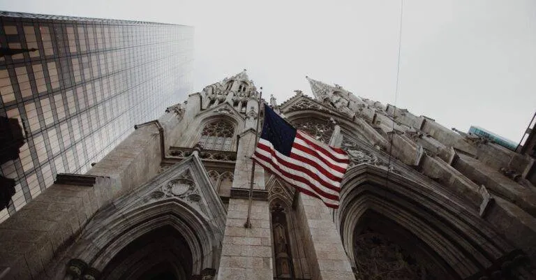 Low Angle View Of American Flag With Historic Cathedral And Skyscraper.