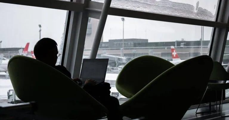 Silhouette Of A Man Working On Laptop At Airport Lounge With Planes Outside.