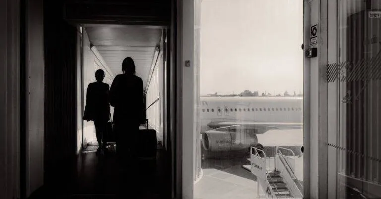 Silhouetted Travelers Walking Through An Airport Jet Bridge Toward An Airplane, Conveying A Travel Mood.