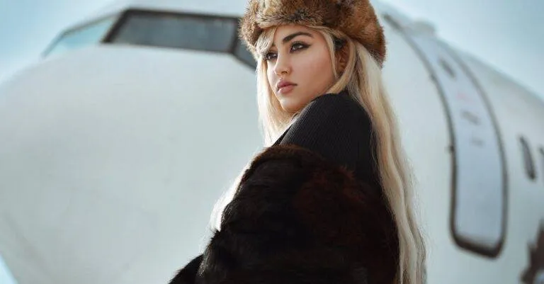 Stylish Woman In Fur And Hat Posing Near Aircraft In Winter Setting.
