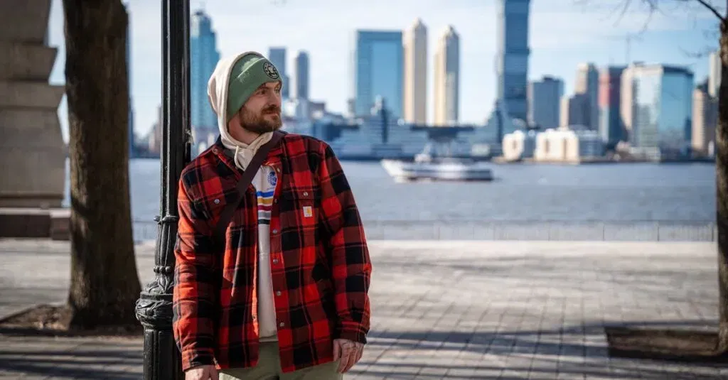 A Man In Casual Winter Attire Stands With Manhattan Skyline In The Background.