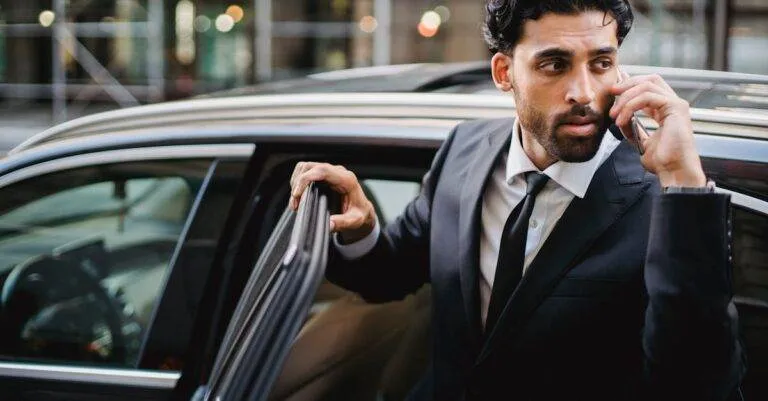 Confident Businessman In A Suit Stepping Out Of A Car While Talking On The Phone.