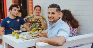 Group Of Friends Enjoying A Meal Together Outdoors At A Cafe, Smiling And Socializing.