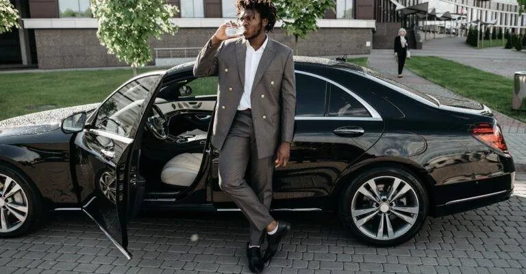 A Fashionable Businessman Stands By A Luxury Car, Enjoying A Drink On A City Street.