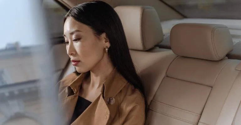 An Elegant Asian Woman Sits Thoughtfully In A Luxurious Car Interior.