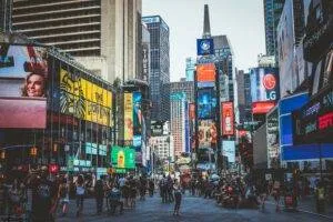 Bustling Daytime View Of Times Square With Crowds, Skyscrapers, And Iconic Billboards In New York City.