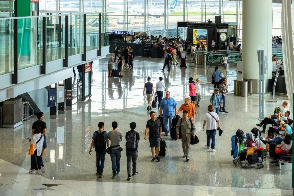 Passengers Walking And Seated In A Bustling Hong Kong Airport Terminal.