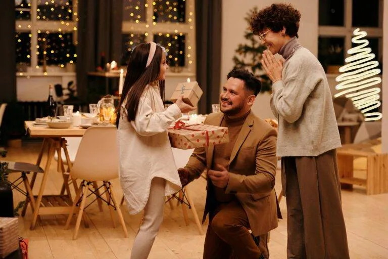 A Joyful Family Exchanging Gifts Indoors During The Christmas Season, Capturing A Moment Of Togetherness.