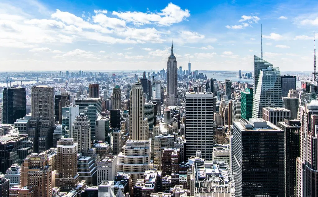 A Stunning Aerial View Of New York City'S Skyline Featuring The Iconic Empire State Building Under A Bright Blue Sky.