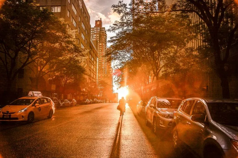 Silhouette Of A Cyclist During Sunset On A New York City Street With Urban Buildings And Cars.