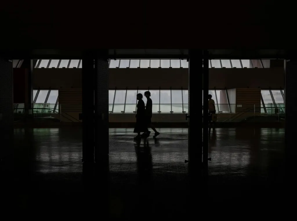 Silhouette Of People Walking Through A Modern Hallway With Large Windows In Shanghai, China.
