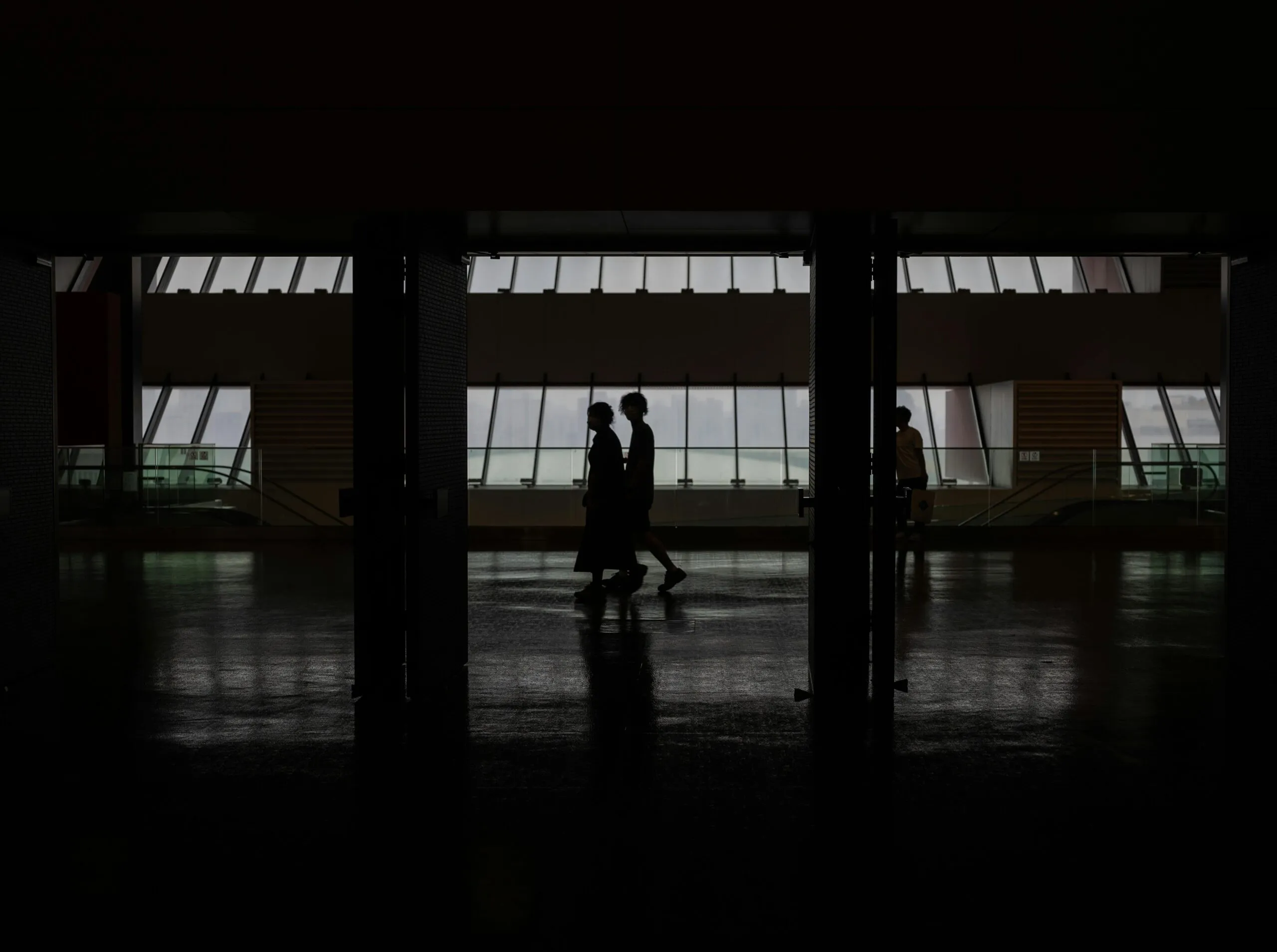 Silhouette Of People Walking Through A Modern Hallway With Large Windows In Shanghai, China.
