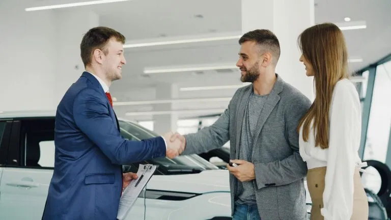 Friendly Handshake Between A Car Salesman And Customers In A Modern Car Showroom.