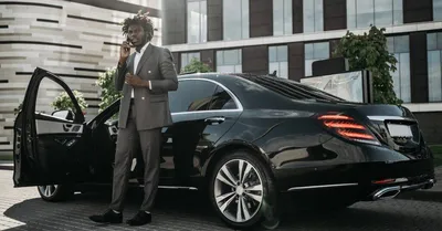 Elegantly Dressed Man In Gray Suit Making Phone Call Next To Sleek Black Car.
