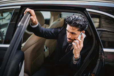 Professional Man In A Suit Exits A Luxury Vehicle During A Phone Call, Emphasizing A Busy Lifestyle.